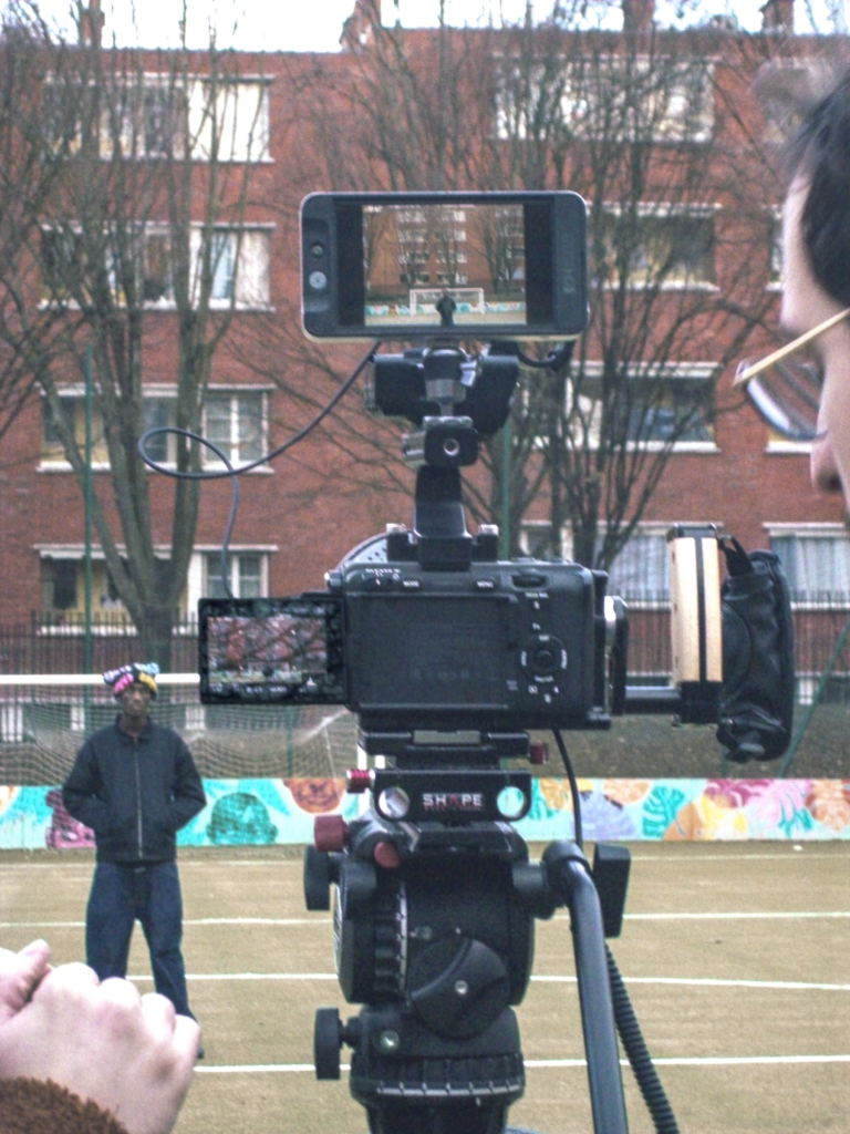 Making Of du tournage du clip avec une caméra au premier plan et l'artiste sur un terrain de foot en arrière plan