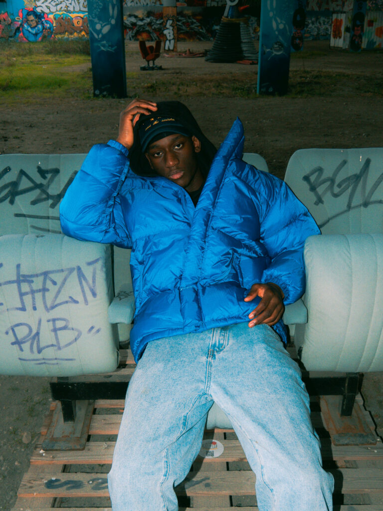 Portrait de l'artiste Izaa assis avec une doudoune bleue